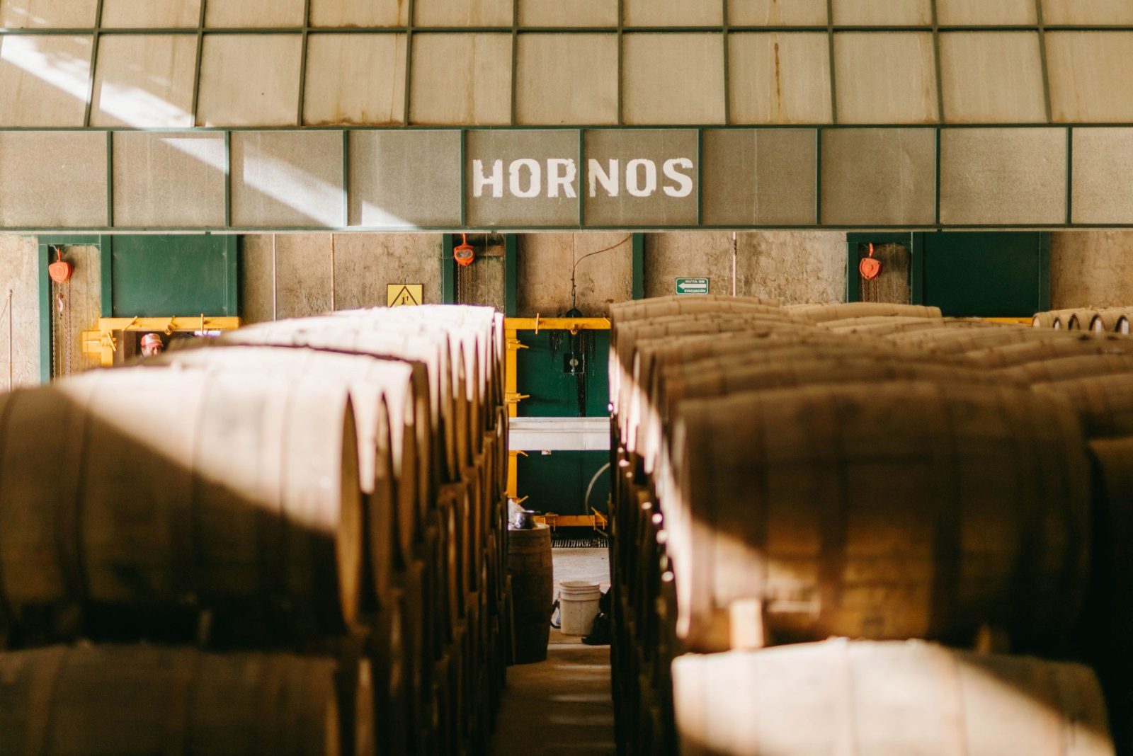Interior view of a tequila factory in Mexico featuring aging barrels beneath 'Hornos' sign.